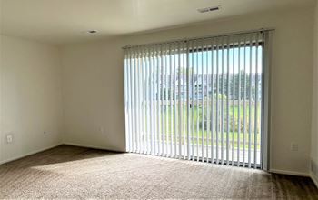 an empty living room with blinds on a window at Windsor Place, Davison, MI